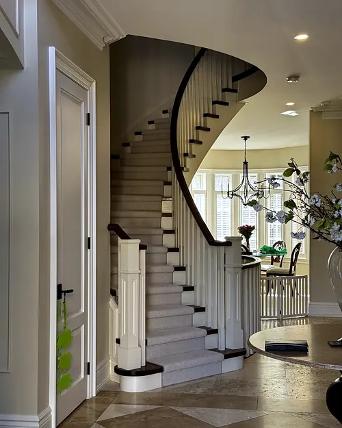Curved staircase with carpeted treads rising from a front hall