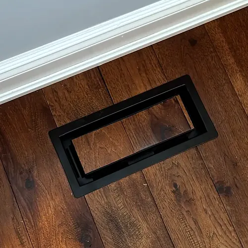 Dark-stained wide plank floor with a flush-mounted floor vent and white baseboard