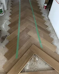 Herringbone floor being laid in a hallway, set out from taped guide lines