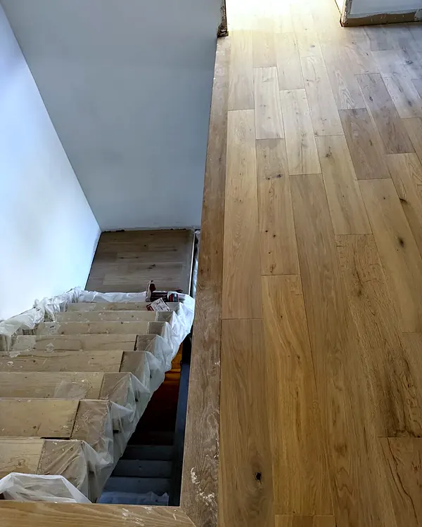 Wide oak plank landing at the top of a staircase, stair treads protected during work